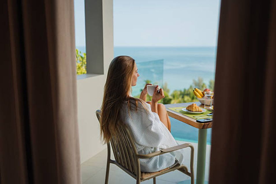Woman enjoying breakfast on a sunny balcony overlooking the sea, feeling like herself