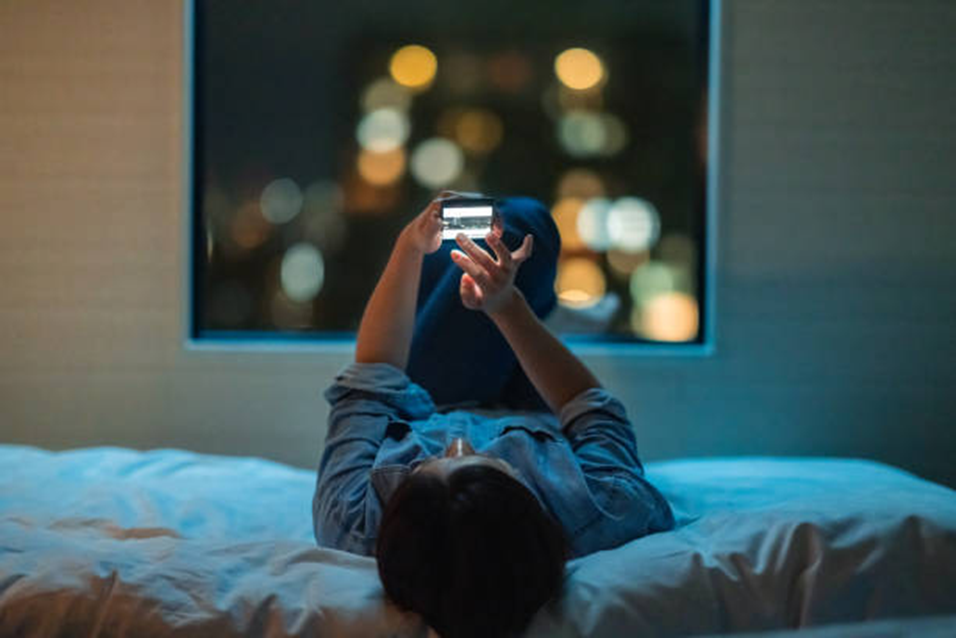 Person lying in bed scrolling a phone at night