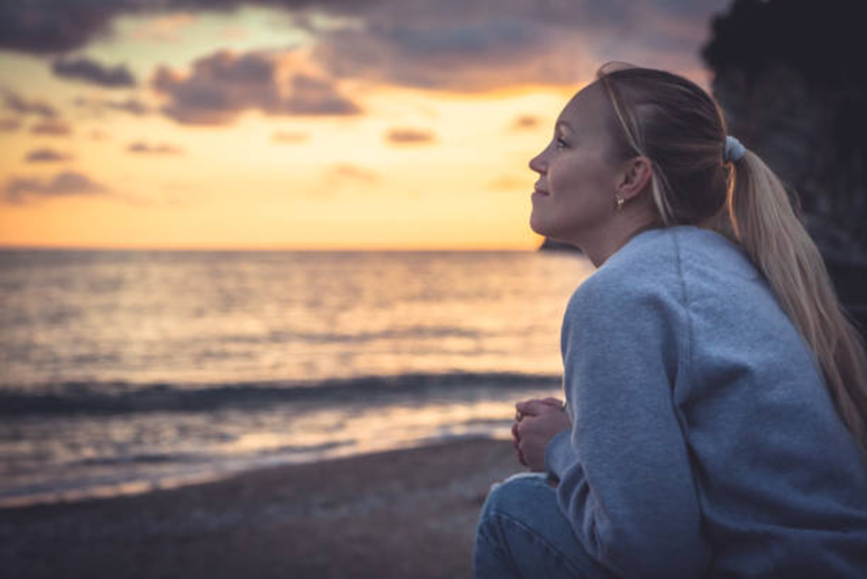 Woman gazing at a sunset over the sea, reflecting honestly on herself