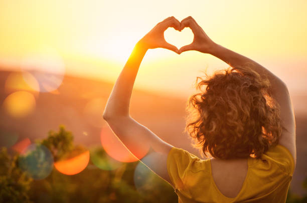 Hands forming a heart shape against the sunset