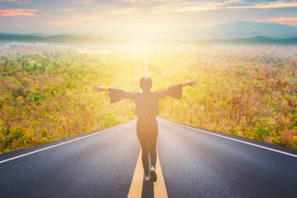 Woman with arms wide open on a sunlit road, beginning a self-healing journey
