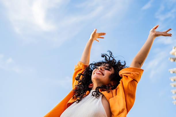 Joyful woman raising her arms under a blue sky