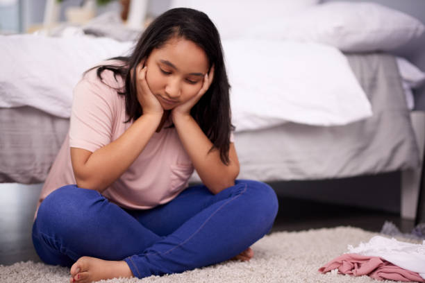 Woman sitting on a bed with her chin in her hands, thinking
